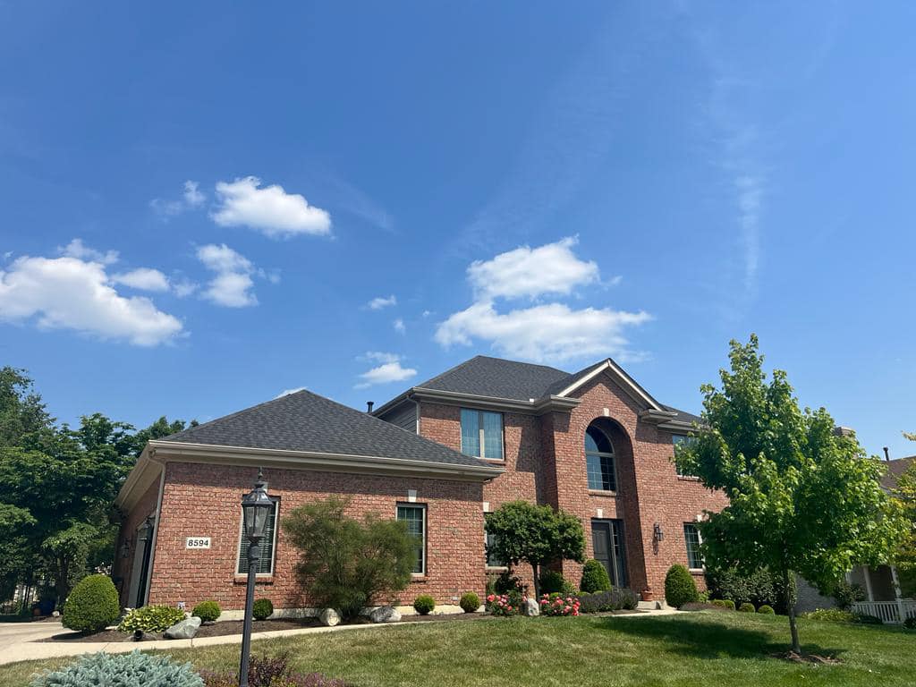 Beautiful two-story red brick house with arched windows, landscaped lawn and mature trees under blue sky