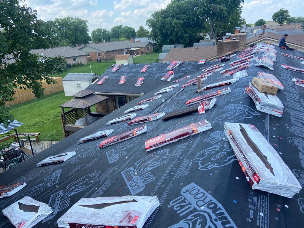 Residential roof replacement in progress with new shingles and underlayment materials scattered across dark roofing surface