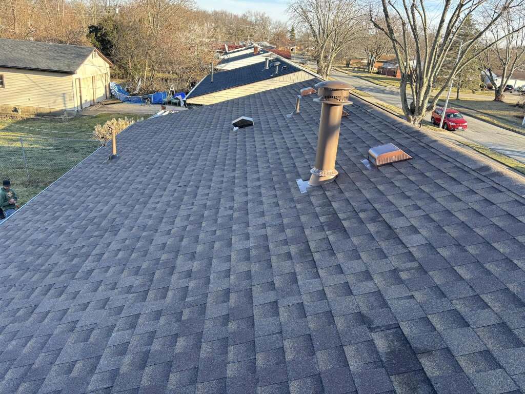 Gray asphalt shingle roof with chimney and vents on residential home in suburban neighborhood setting