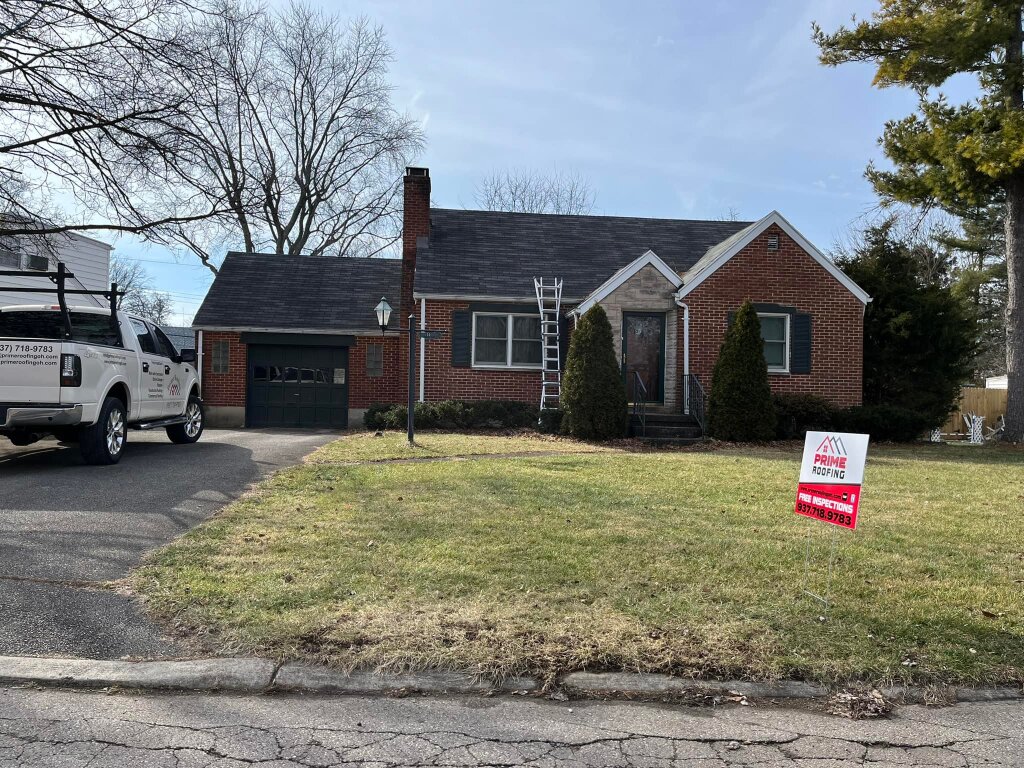 Brick ranch house with dark roof under repair, white contractor truck parked in driveway, Prime Roofing sign