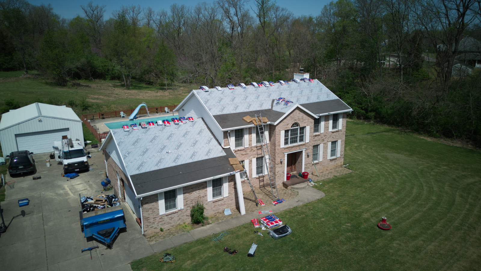 Aerial view of two-story brick house under construction with new roof installation, surrounded by green lawn
