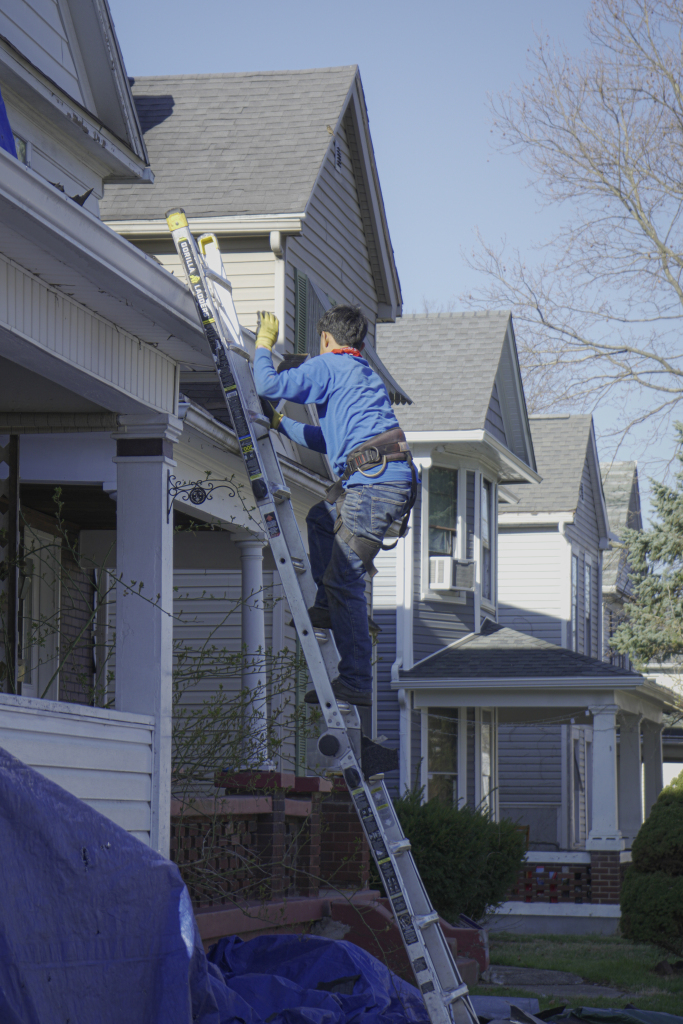 Professional worker in blue uniform climbing ladder to perform home maintenance on residential house exterior