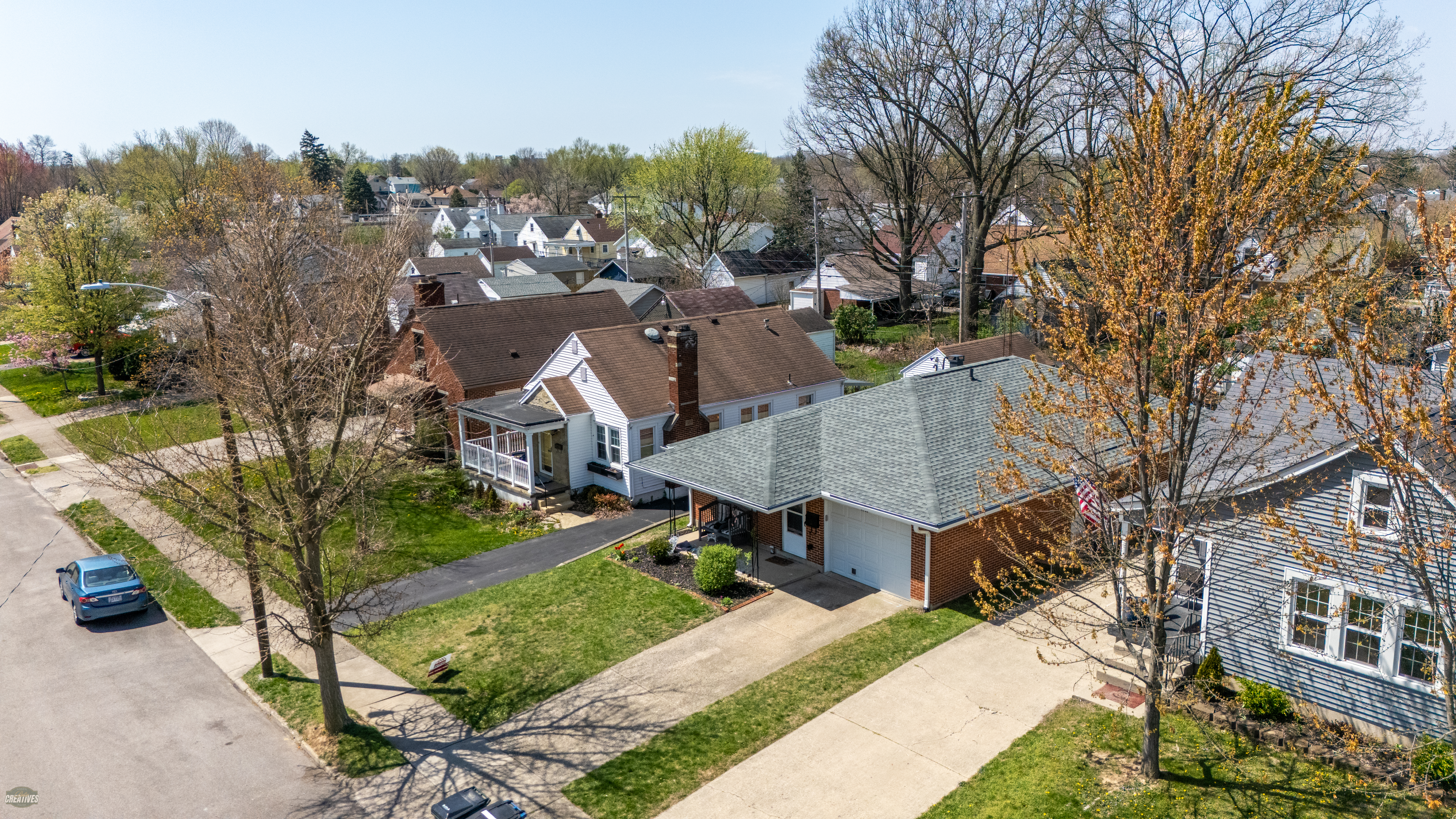 Aerial view of suburban neighborhood with white and brick houses, green lawns, mature trees in spring foliage