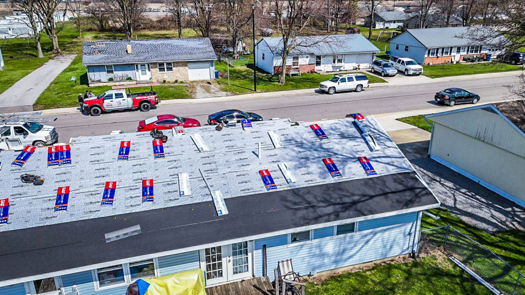 Aerial view of residential roof replacement with red and blue shingle bundles scattered across roof surface