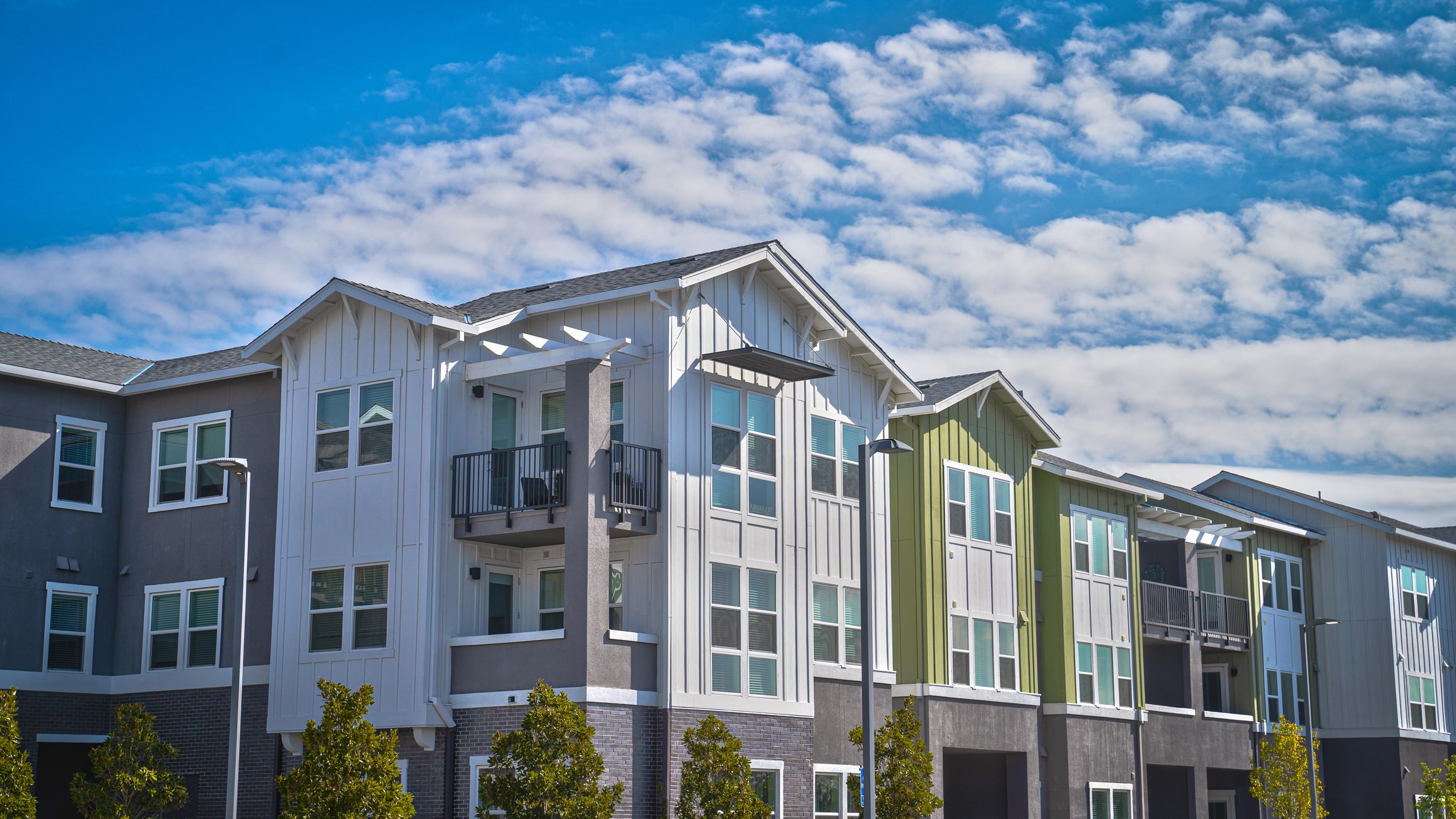 Modern townhouses with colorful siding and balconies under blue sky with white clouds in residential development