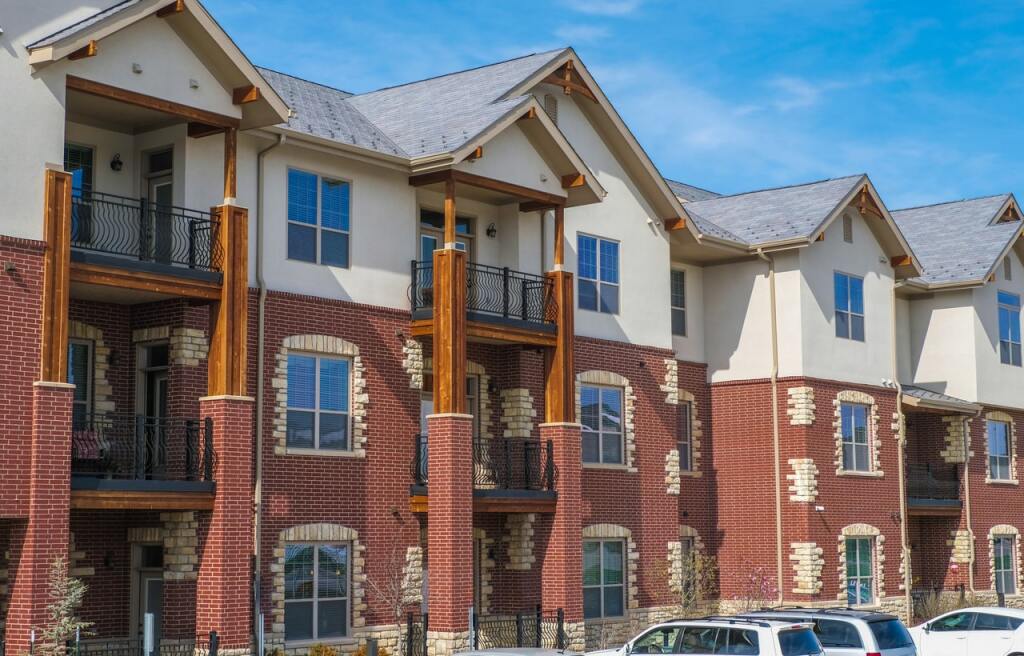 Modern residential townhouses with red brick, white stucco, and wood accents featuring balconies under blue sky