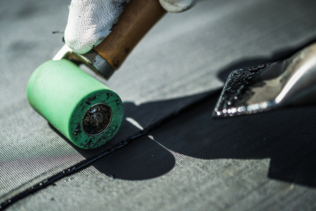 Hand in white glove using green paint roller to apply black paint on wooden surface during home renovation