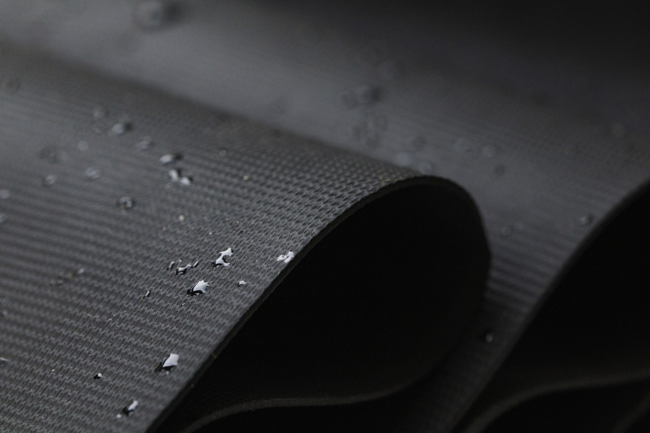 Black waterproof fabric with water droplets beading on textured surface showing water-resistant properties