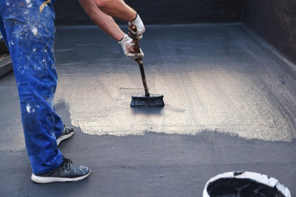 Worker in blue coveralls applying waterproof coating to concrete surface with brush during construction work