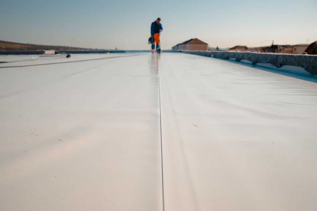 Worker in blue shirt and orange pants standing on white flat roof during installation or maintenance work