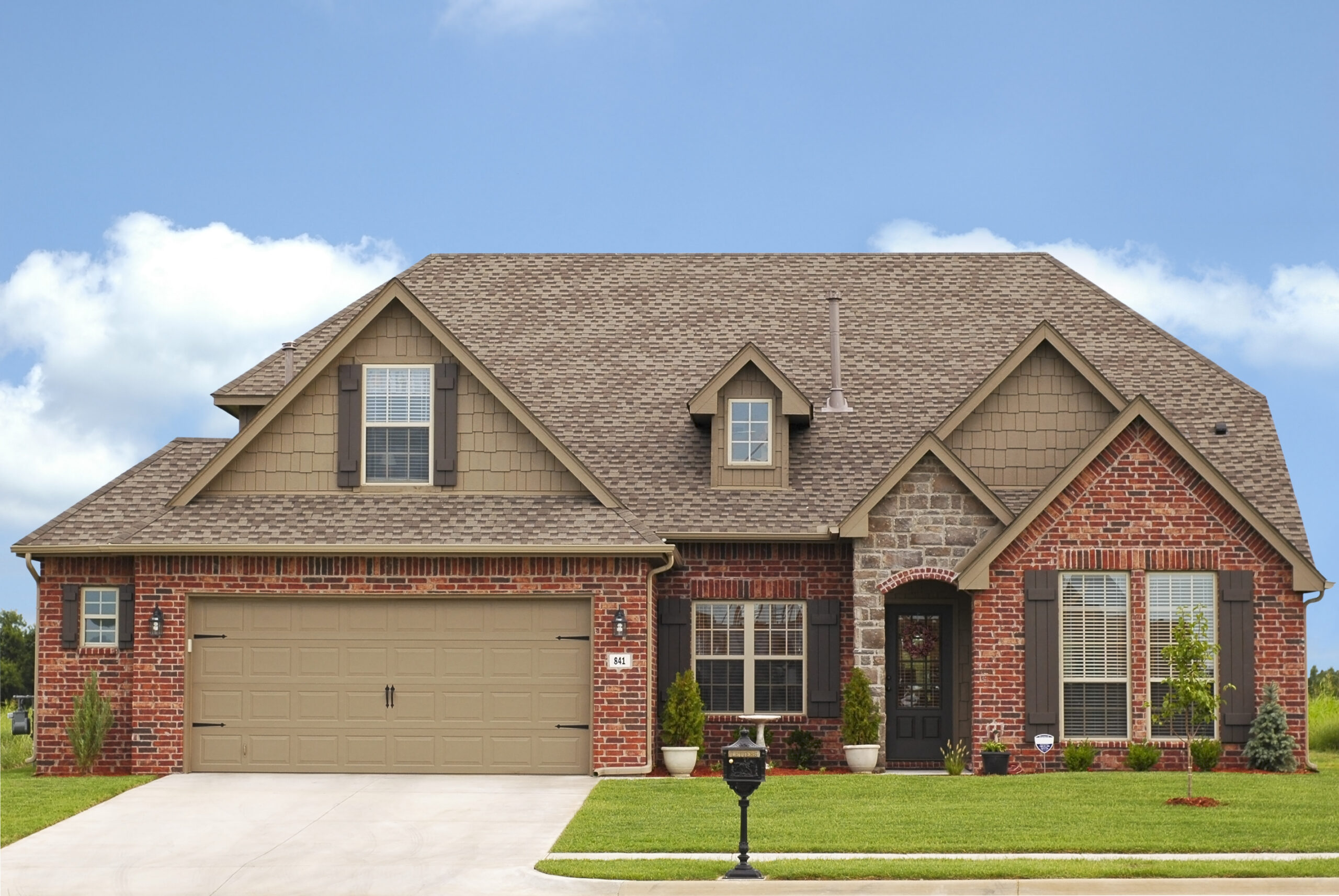 Modern single-family brick home with beige siding, brown shingle roof, two-car garage, and manicured lawn