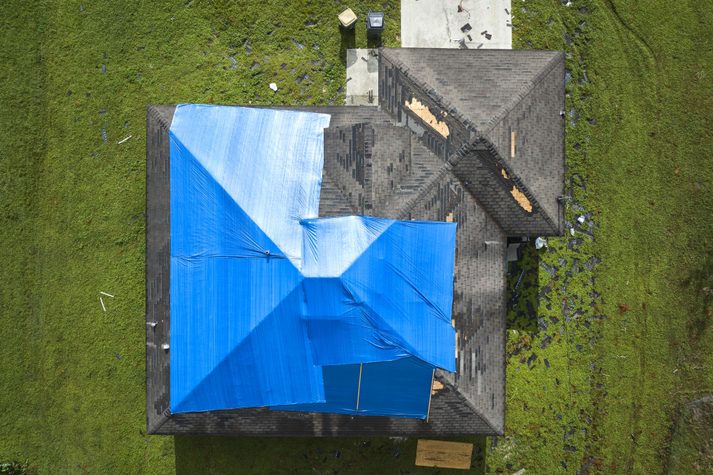Aerial view of residential house roof covered with bright blue protective tarp alongside gray shingles