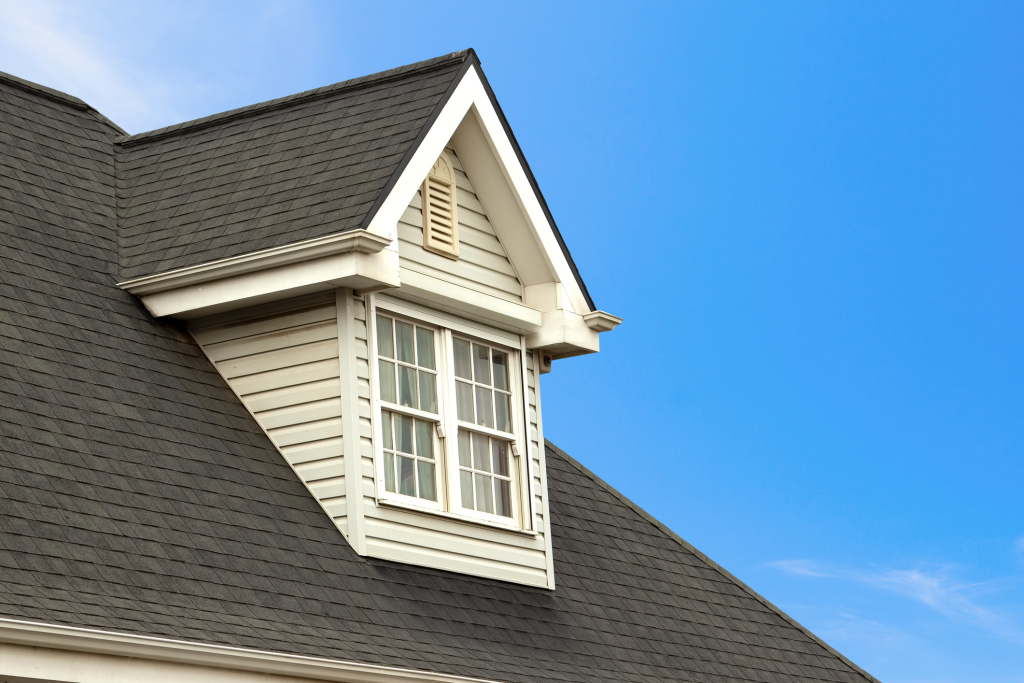 House dormer window with white siding and grid-pattern glass on dark gray shingle roof against blue sky