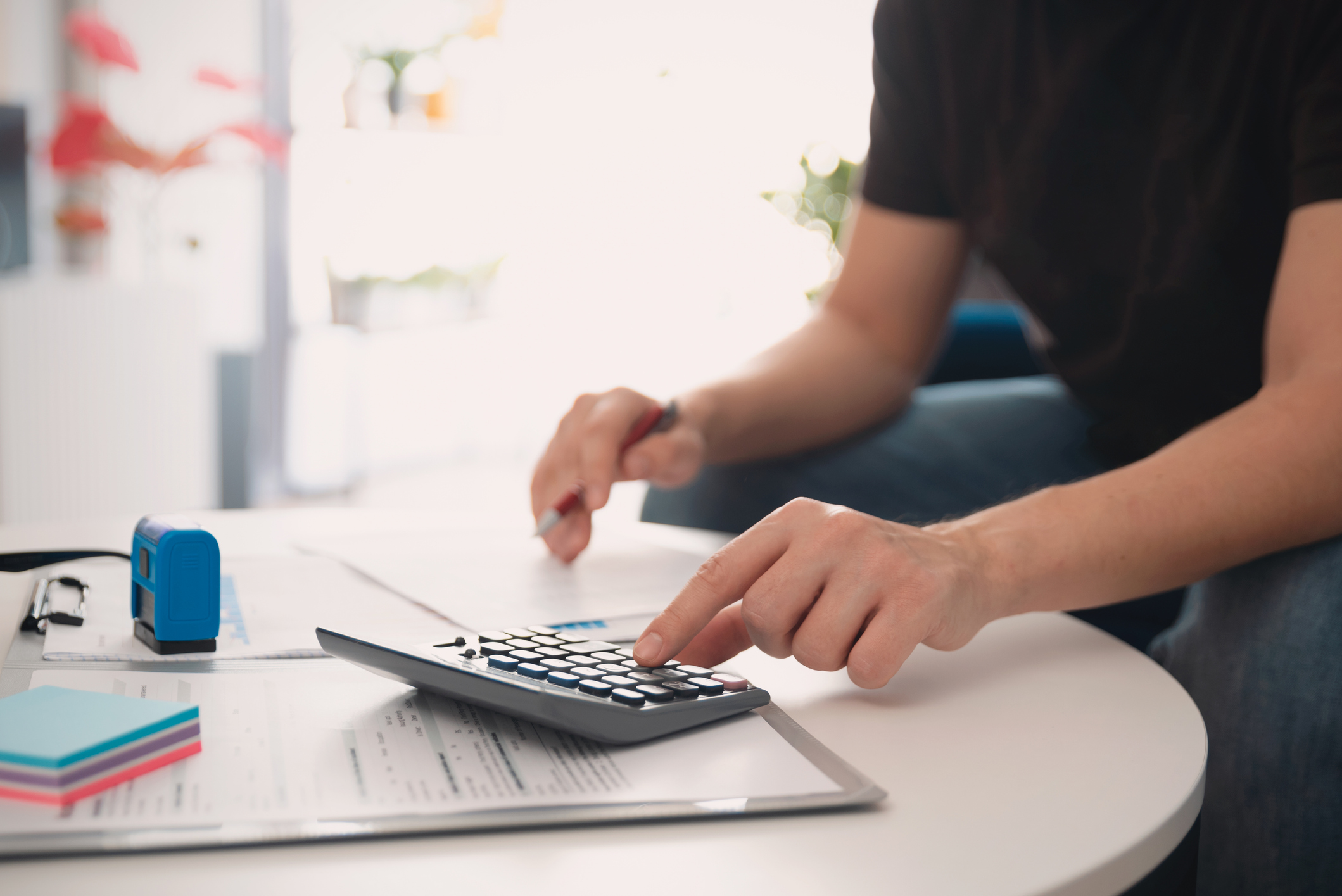 Person using calculator at white desk with financial documents and office supplies for accounting work