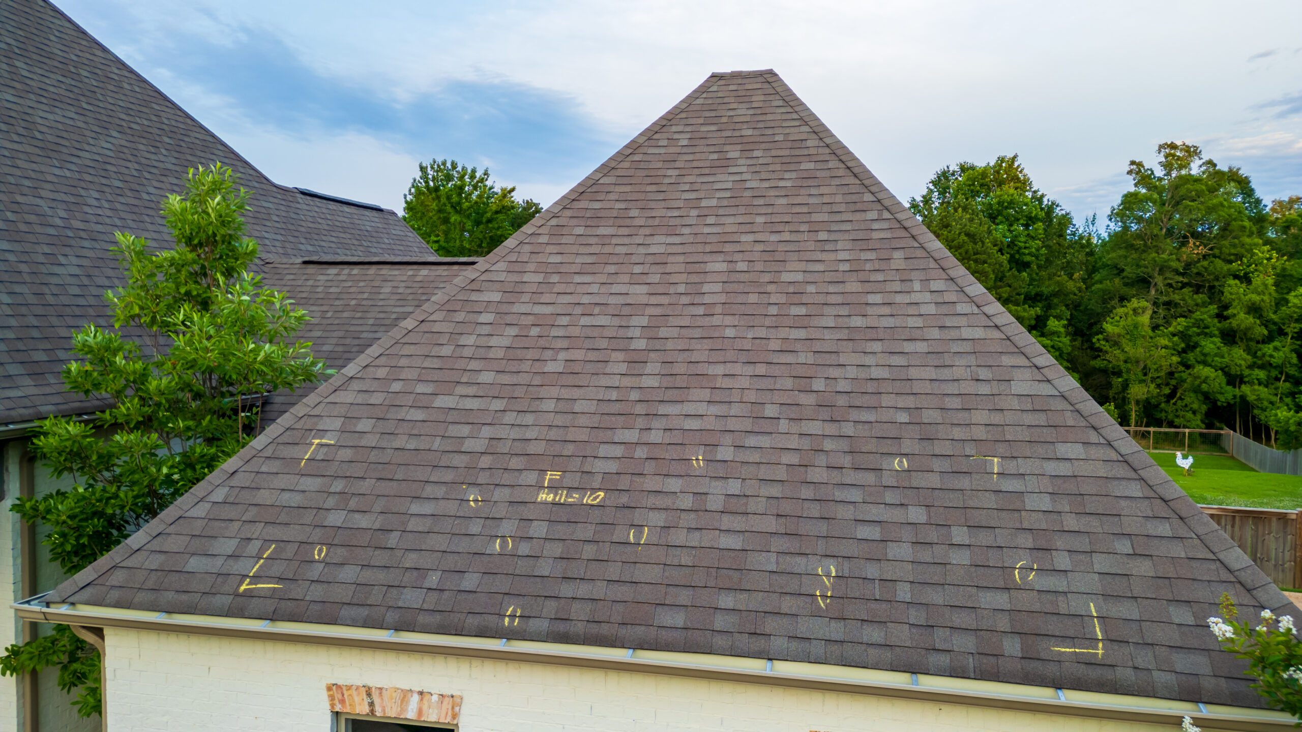 Steep triangular shingled roof with yellow chalk markings showing repair areas, surrounded by green trees