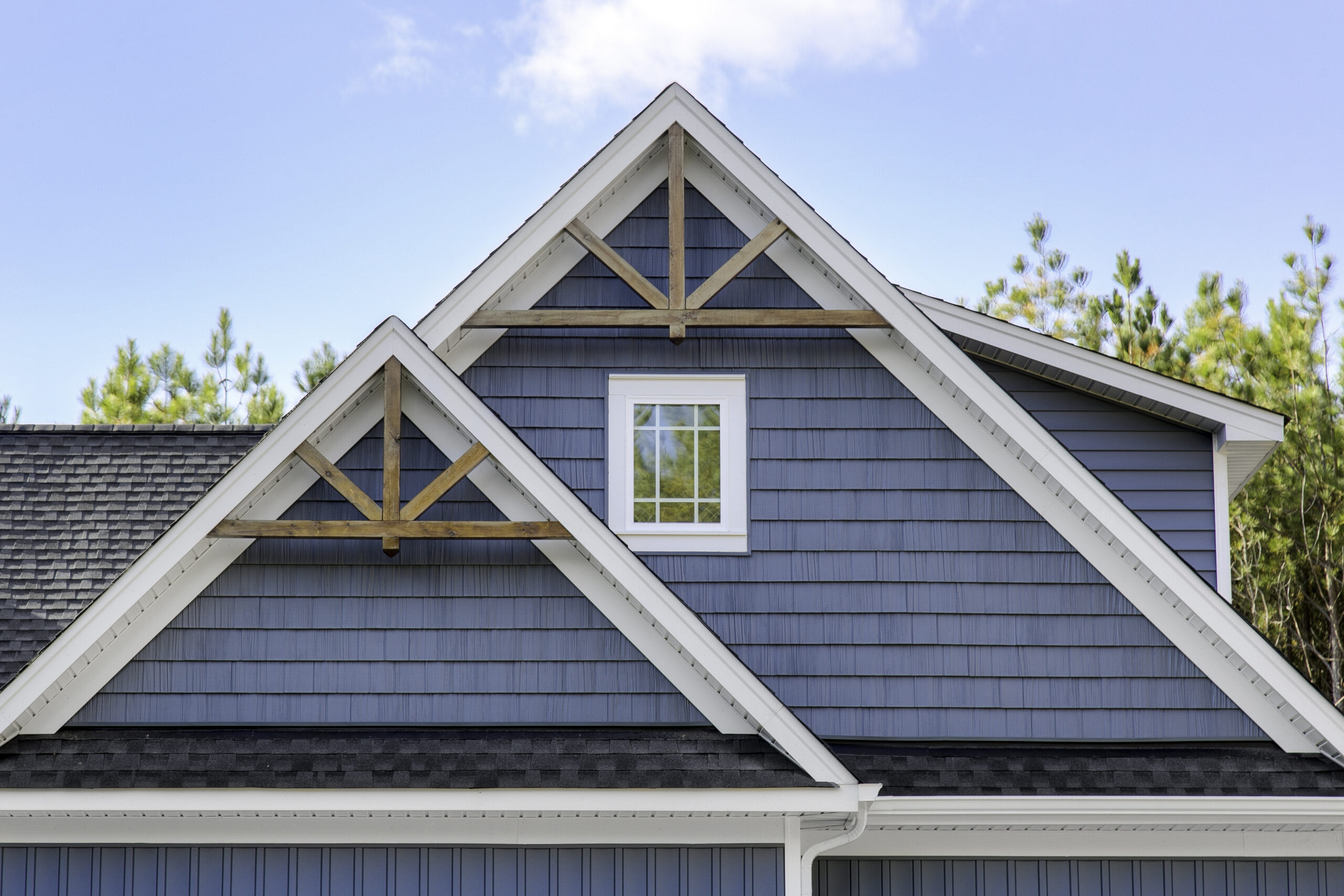 Blue cedar shake siding house with white trim featuring triangular gable peaks and decorative timber accents