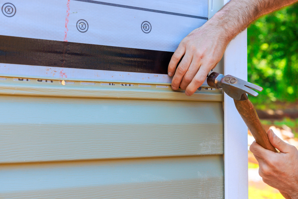 Person hammering nails into light blue painted wood siding during exterior home installation or repair work