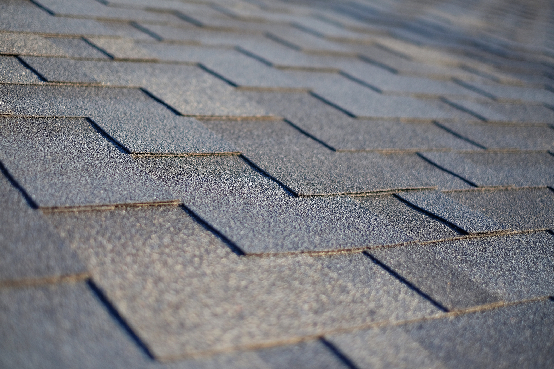 Close-up of gray asphalt roof shingles showing overlapping pattern and textured surface on residential home
