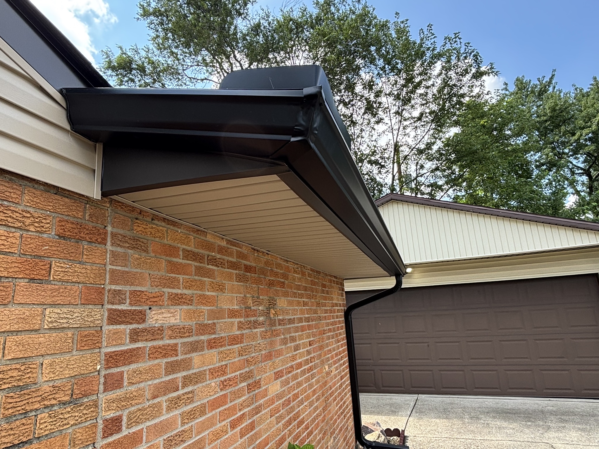 Modern house exterior with dark gutters, brick wall, and brown garage door surrounded by green trees