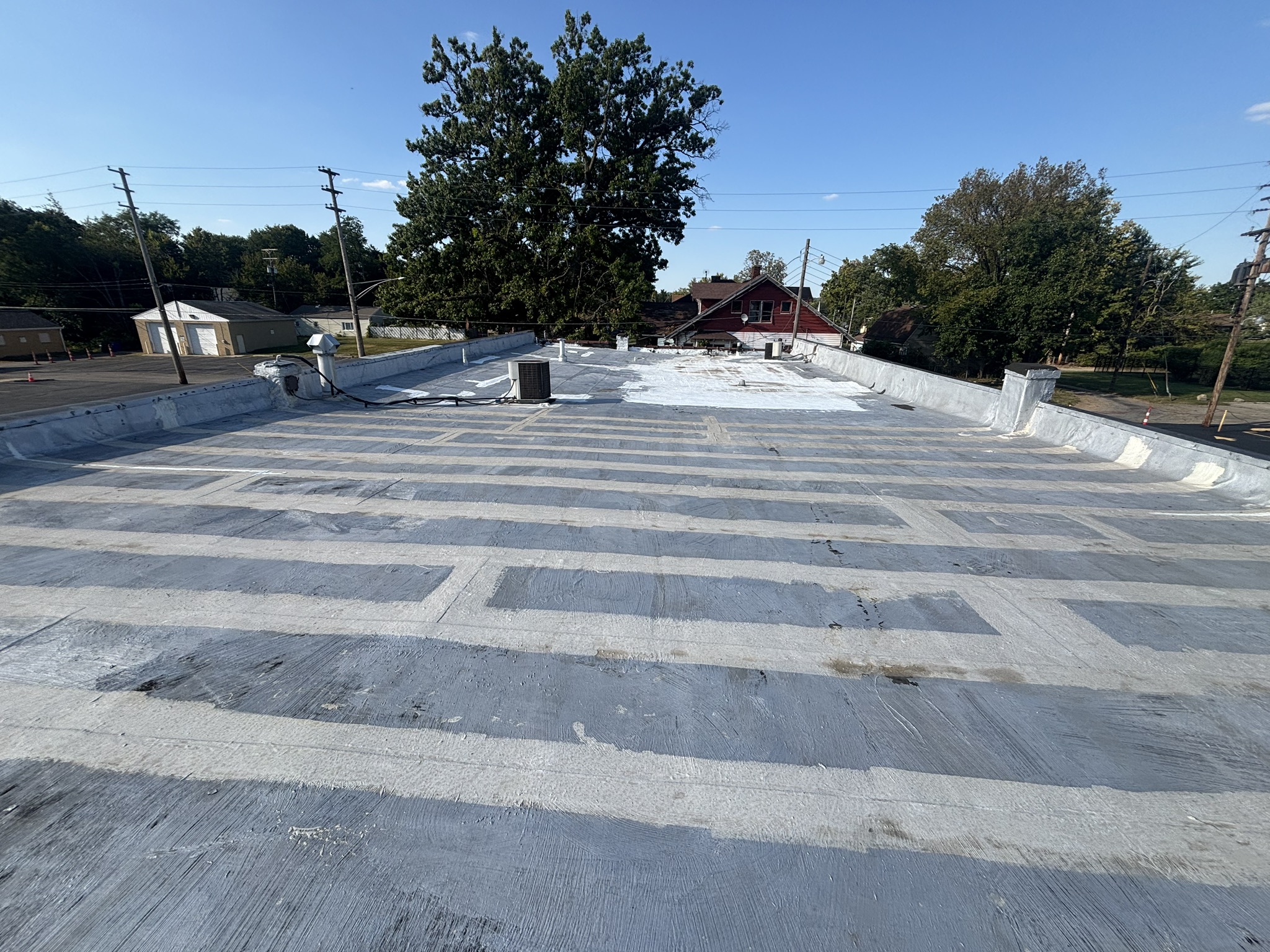 Flat commercial roof with white membrane roofing system, HVAC unit, and residential neighborhood in background