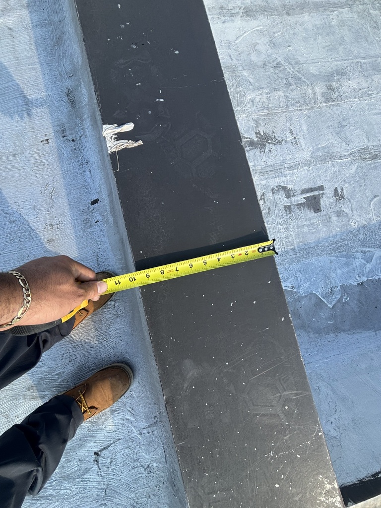 Person measuring black roofing material with yellow tape measure on construction site from overhead view