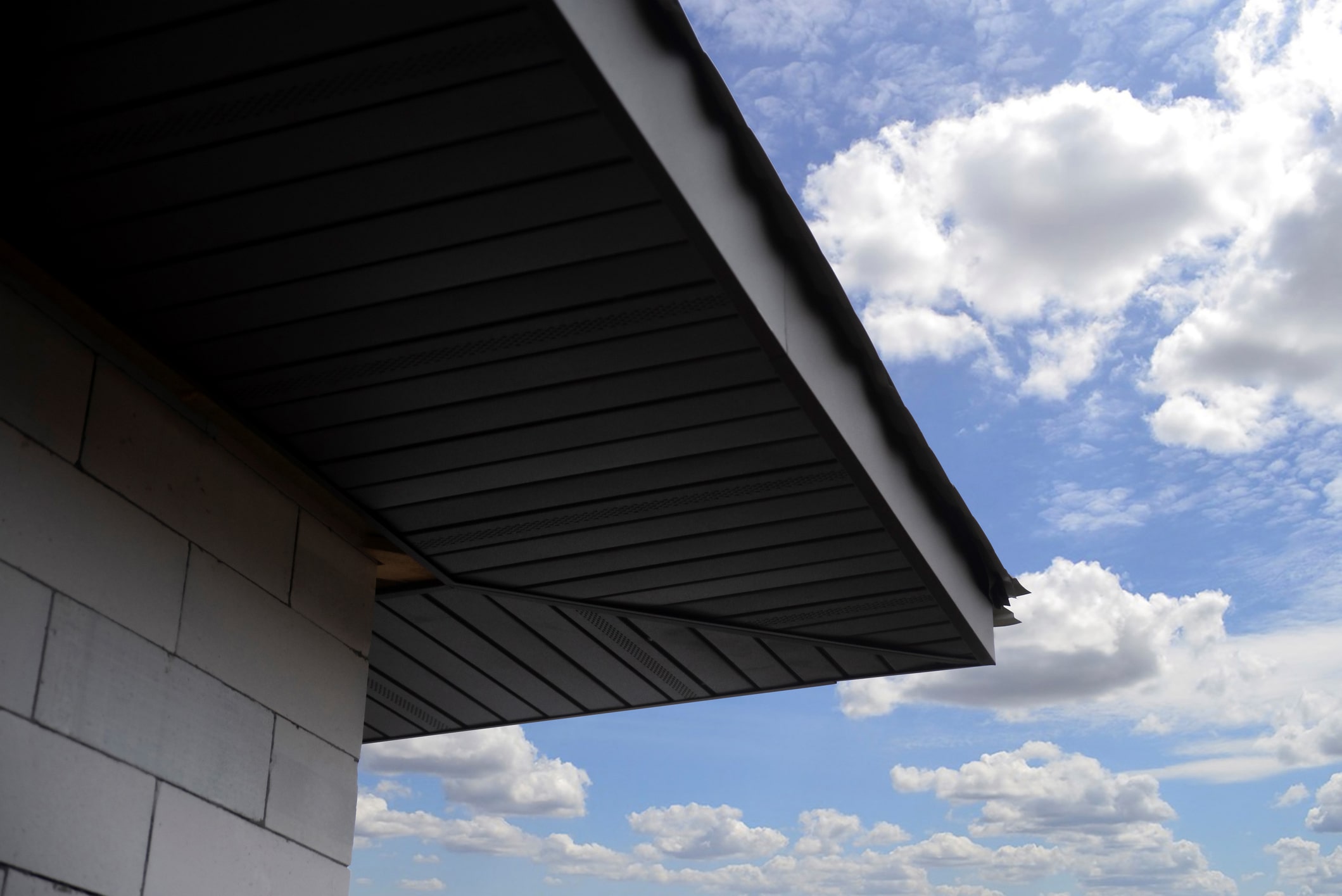 Modern building exterior with geometric overhang against blue sky with white puffy clouds