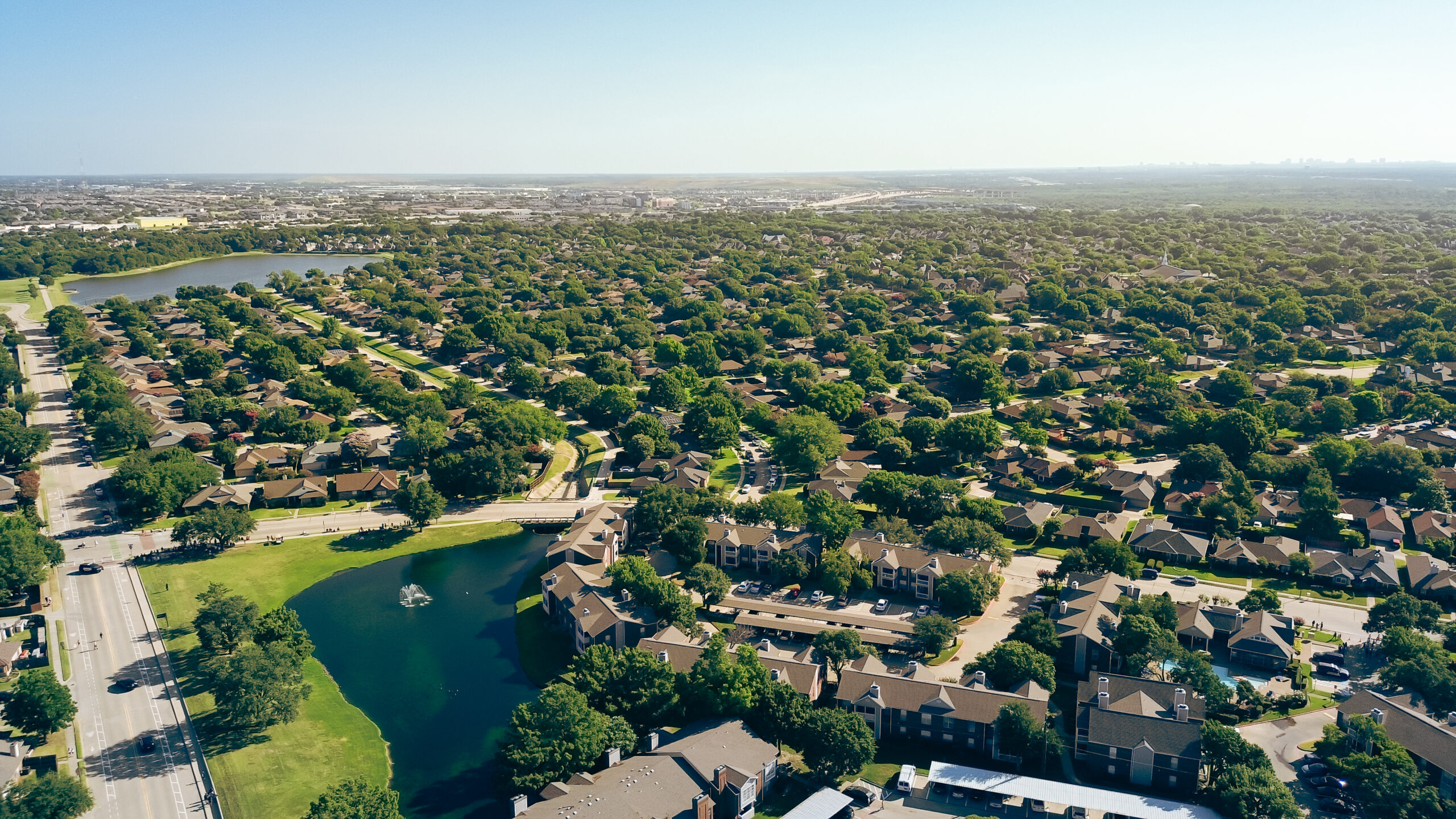 Aerial view of suburban residential neighborhood with lake, tree-lined streets, and houses extending to horizon