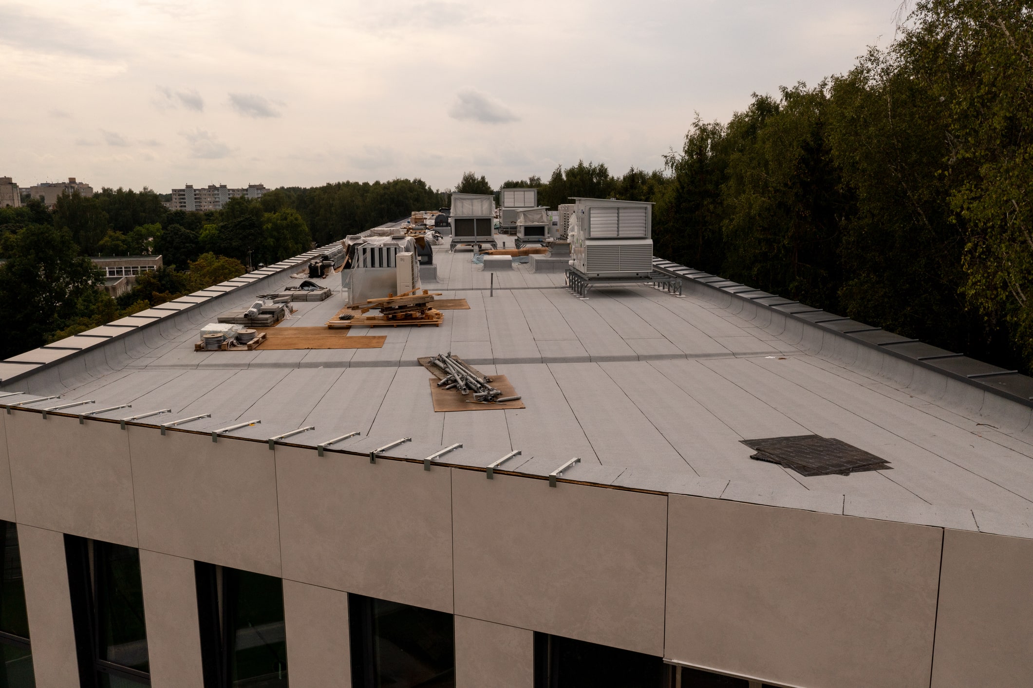 Commercial building flat roof with HVAC units, construction materials, and safety railings under cloudy sky