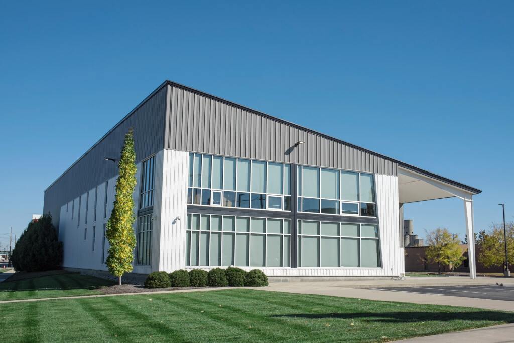 Modern commercial building with gray metal siding, large glass windows, and white covered entrance area