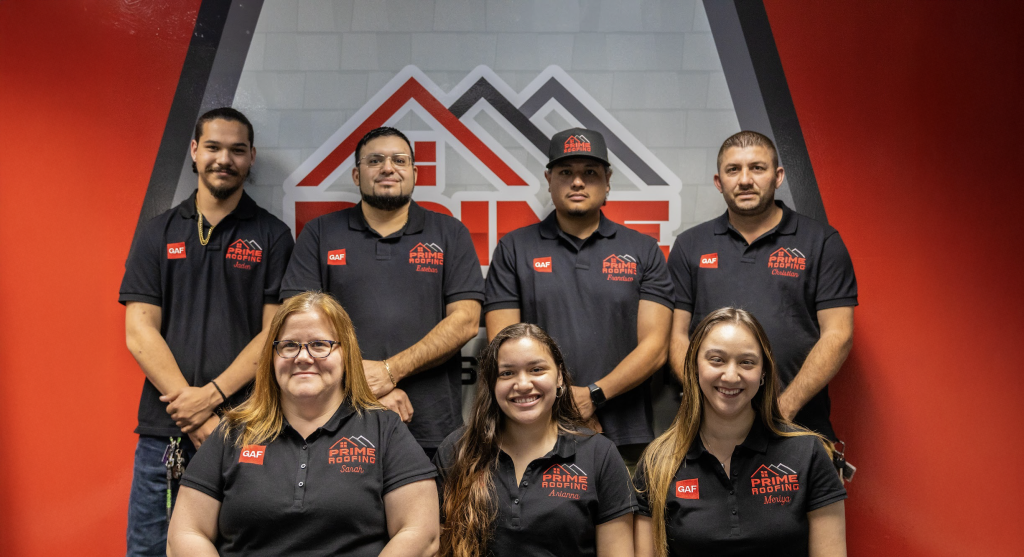 Seven Prime Roofing team members in matching black polo shirts posing together in front of company logo wall