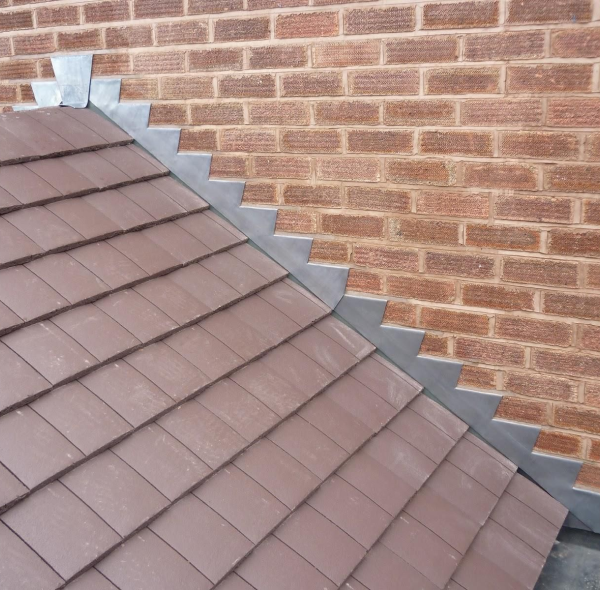 Gray metal roof flashing installed along red brick wall edge with brown clay tile roofing system