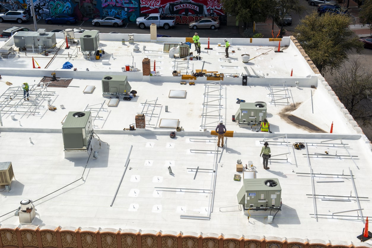 Aerial view of commercial building rooftop construction site with workers in safety vests installing HVAC units