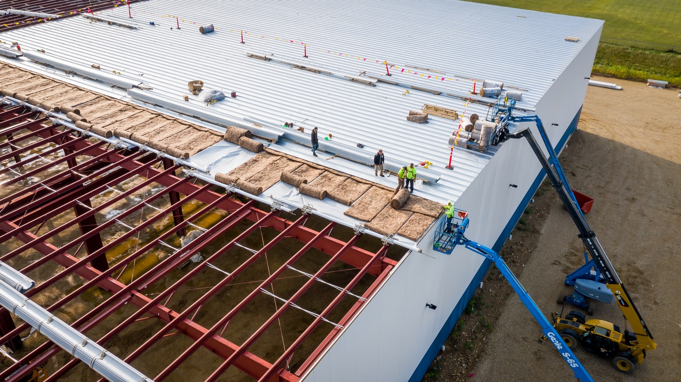 Aerial view of commercial roof construction with workers installing metal panels and insulation on steel frame