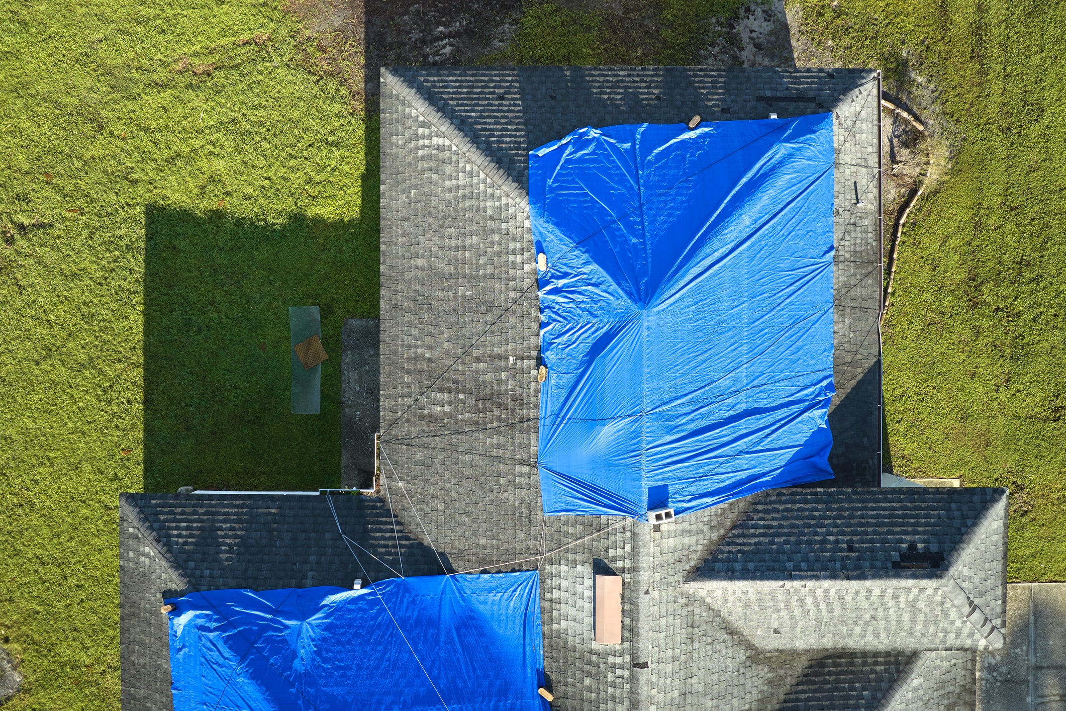 Aerial view of house with blue tarps covering damaged roof sections surrounded by green lawn