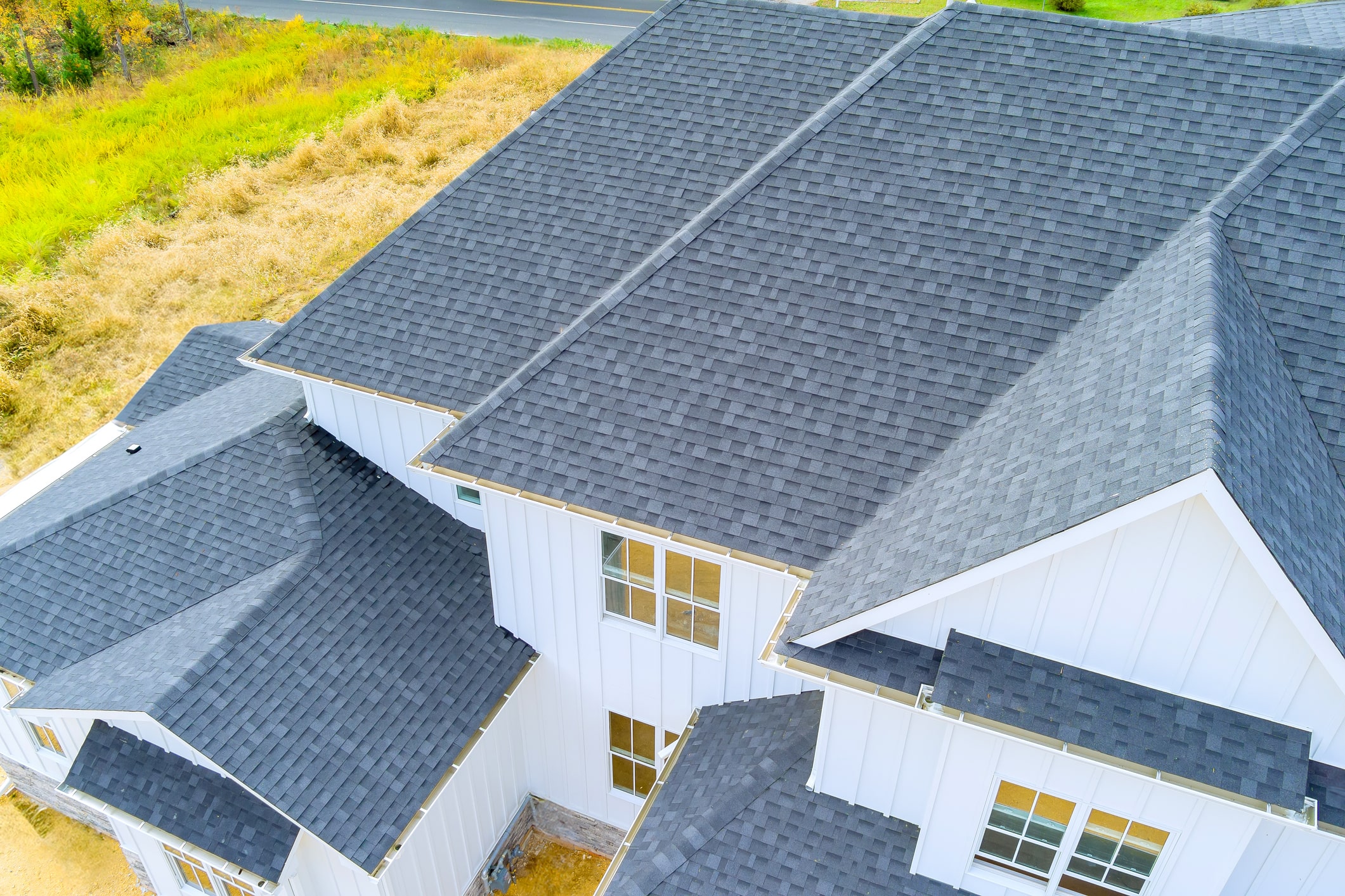 Aerial view of modern residential home with dark gray asphalt shingle roof and white siding exterior
