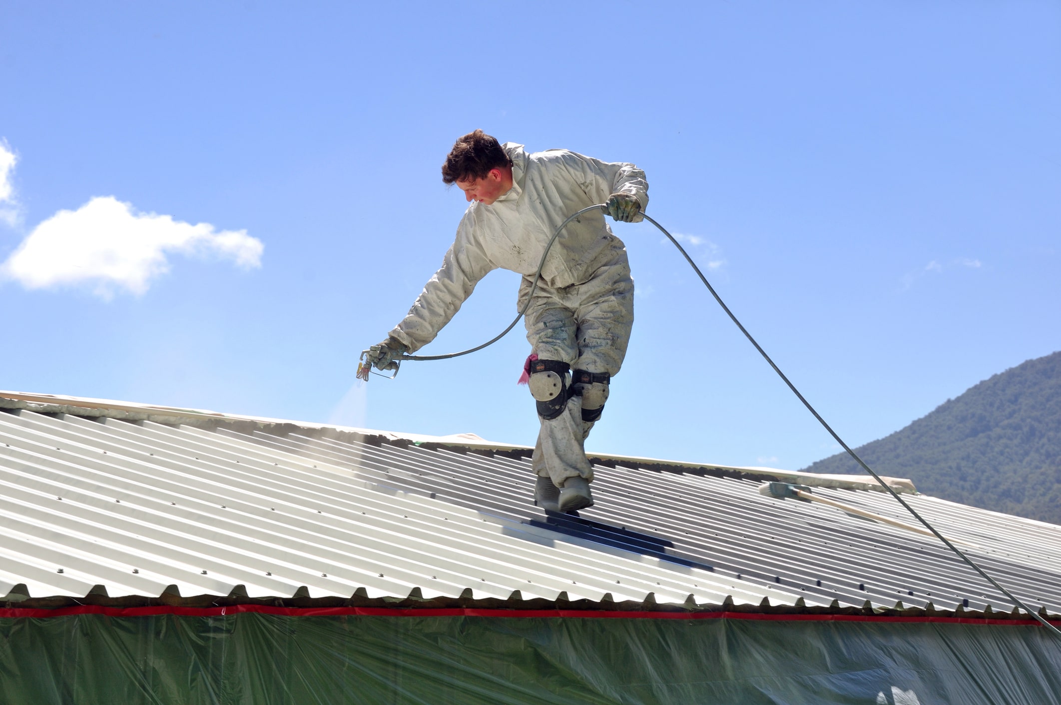 Construction worker in safety gear walking on corrugated metal roof with safety rope against blue sky